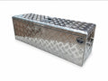 A rectangular aluminum toolbox with a diamond plate pattern, featuring a lid, side handles, set against a plain white background.