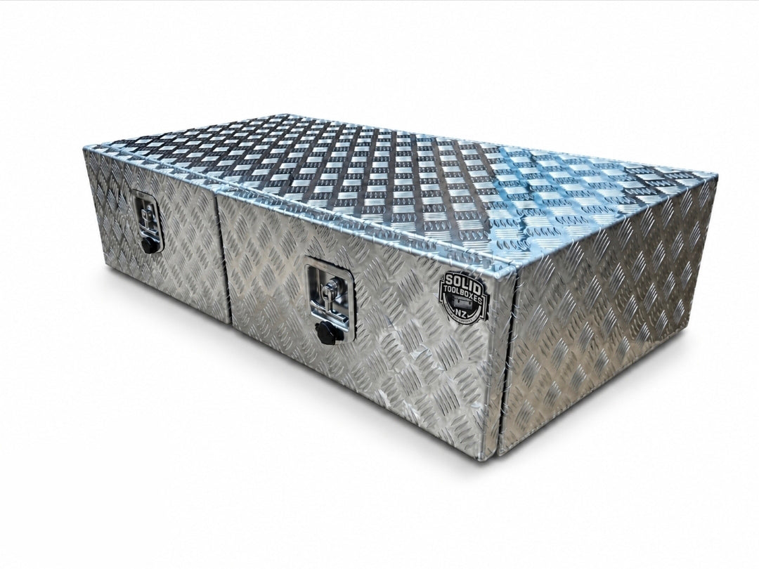 A rectangular aluminum toolbox with diamond plate texture, featuring two front lockable compartments and a top lid, shown on a plain white background.