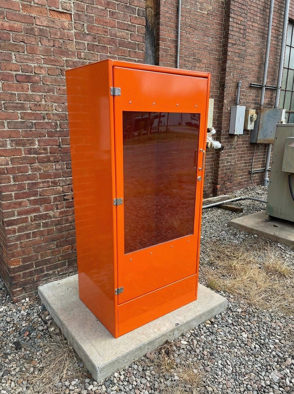 Orange powdercoated aluminium fire hydrant riser cabinet installed against a brick wall